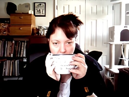 Deb facing the computer holding a coffee cup to her lips